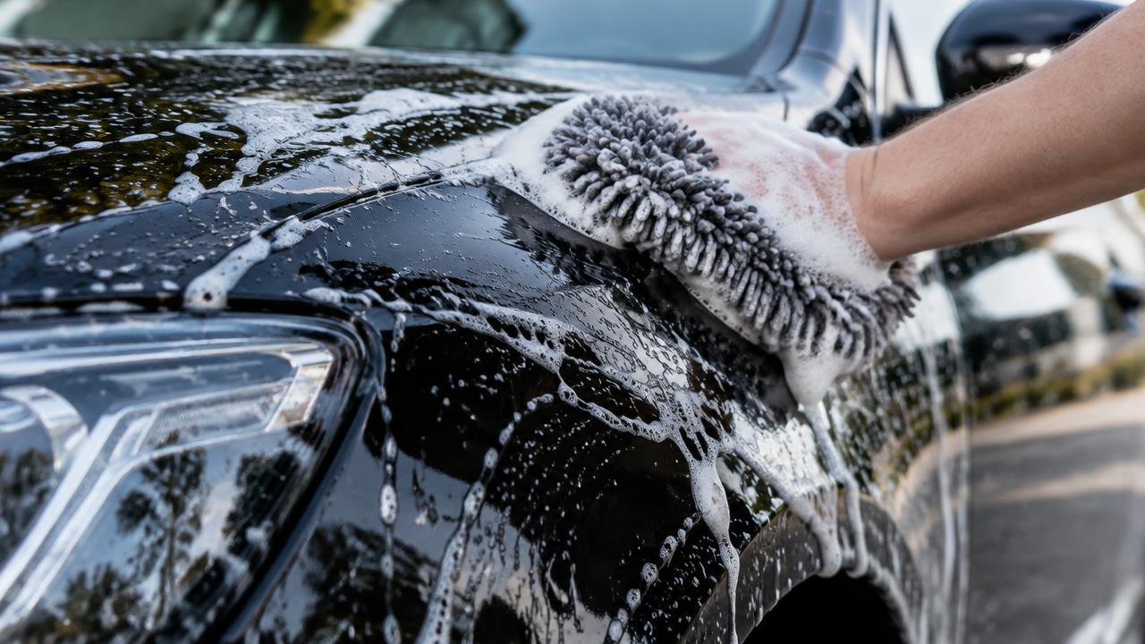 Lavage à la main d'une carrosserie noire avec gant microfibre